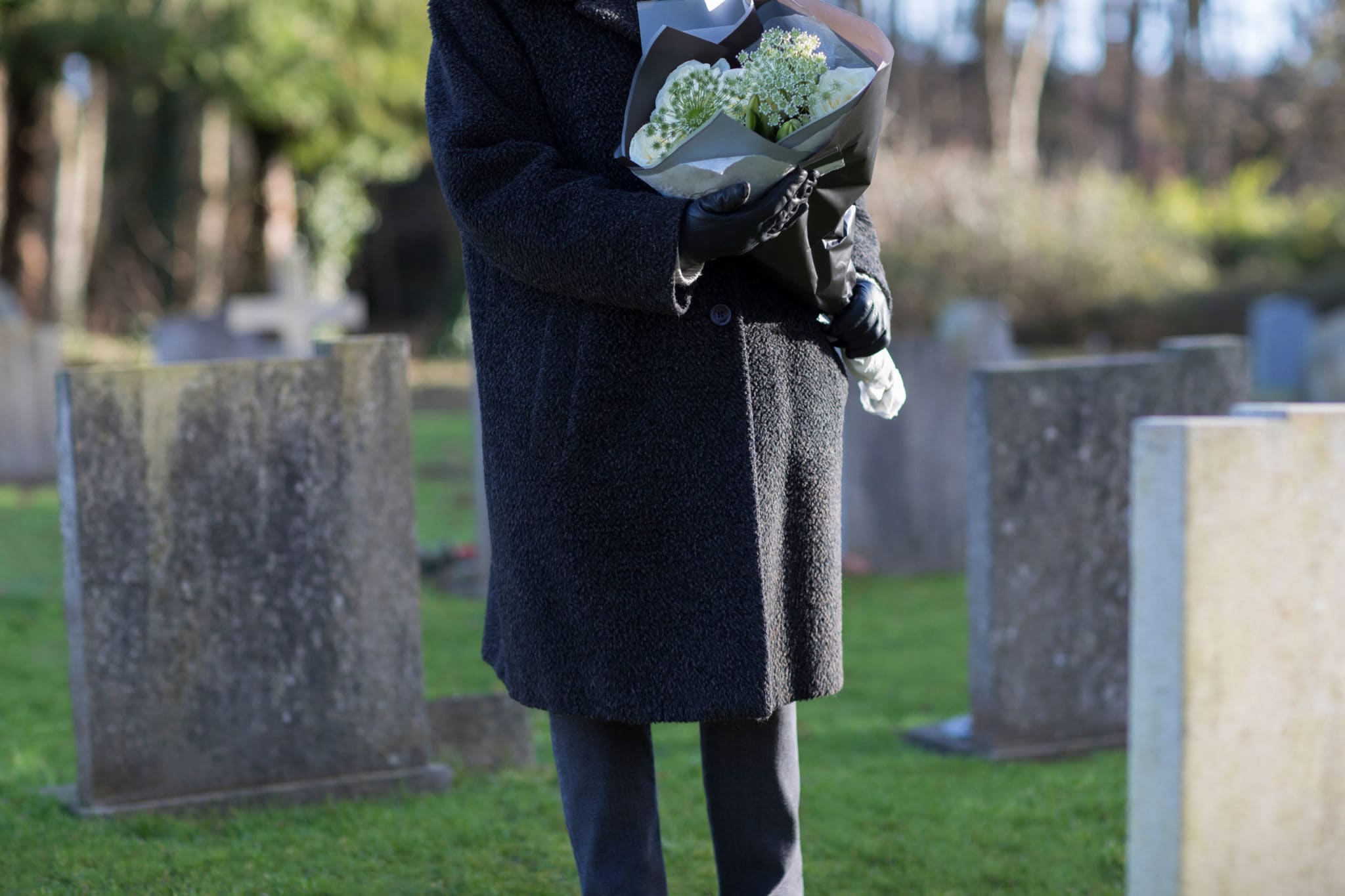 94277719 - close up of senior woman with flowers standing by grave