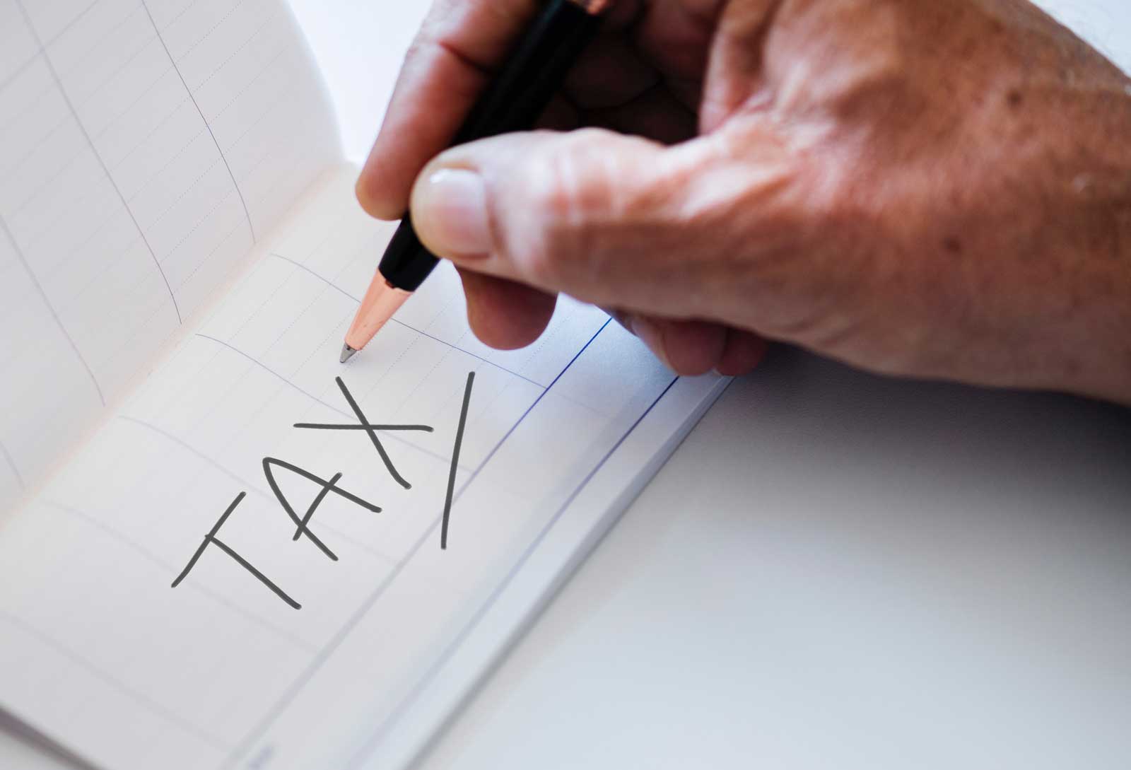 a hand writing "TAX" with an underline