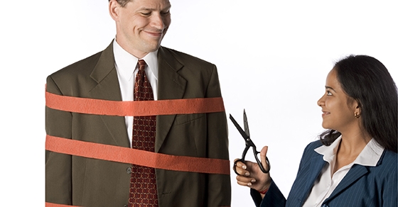 Woman cutting co-worker free from red tape