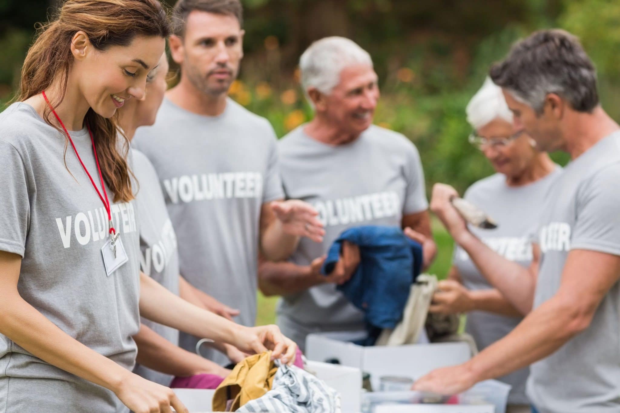 70s; senior; elderly; man; male; caucasian; 60s; woman; female; 40s; mature adult; 30s; mid adult; countryside; nature; environment; activity; recreation; leisure; lifestyle; summer; summertime; sunny; sunshine; happy; smiling; cheerful; community; outreach; volunteer; charity; selfless; concern; care; participate; volunteering; participation; participating; welfare; social; altruism; volunteerism; altruistic; moral; group; together; team; teamwork; holding; box; donations; organizing; event; outdoors;