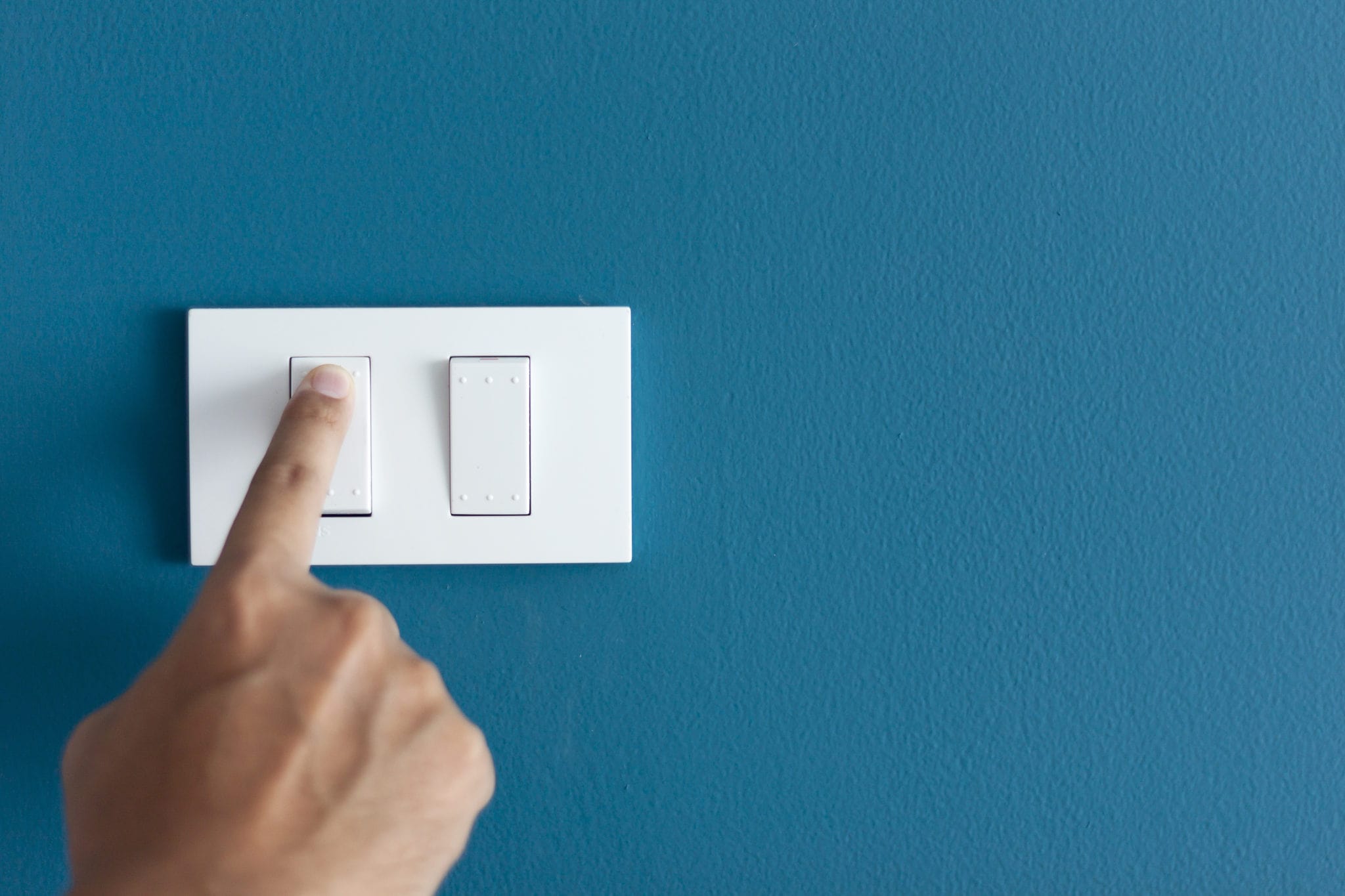 A finger turning on lighting switch on rough on blue dark wall.