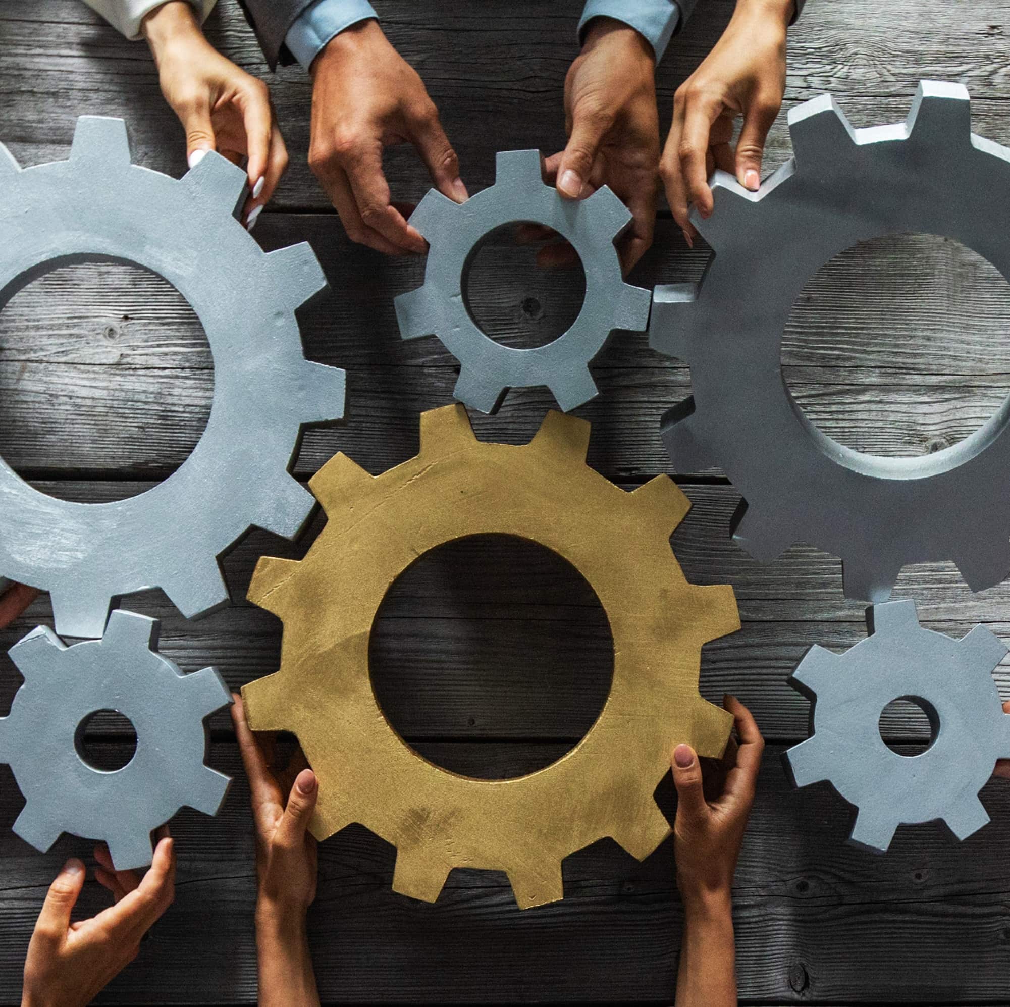 Group of business people joining together silver and golden colored gears on table at workplace top view