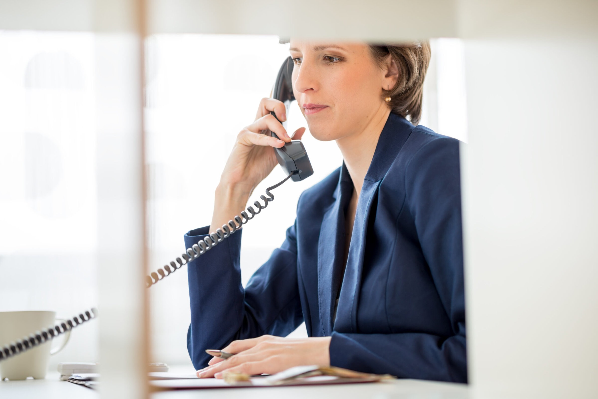 Serious Young Businesswoman Sitting at her Desk Answering a Telephone Call from a Customer