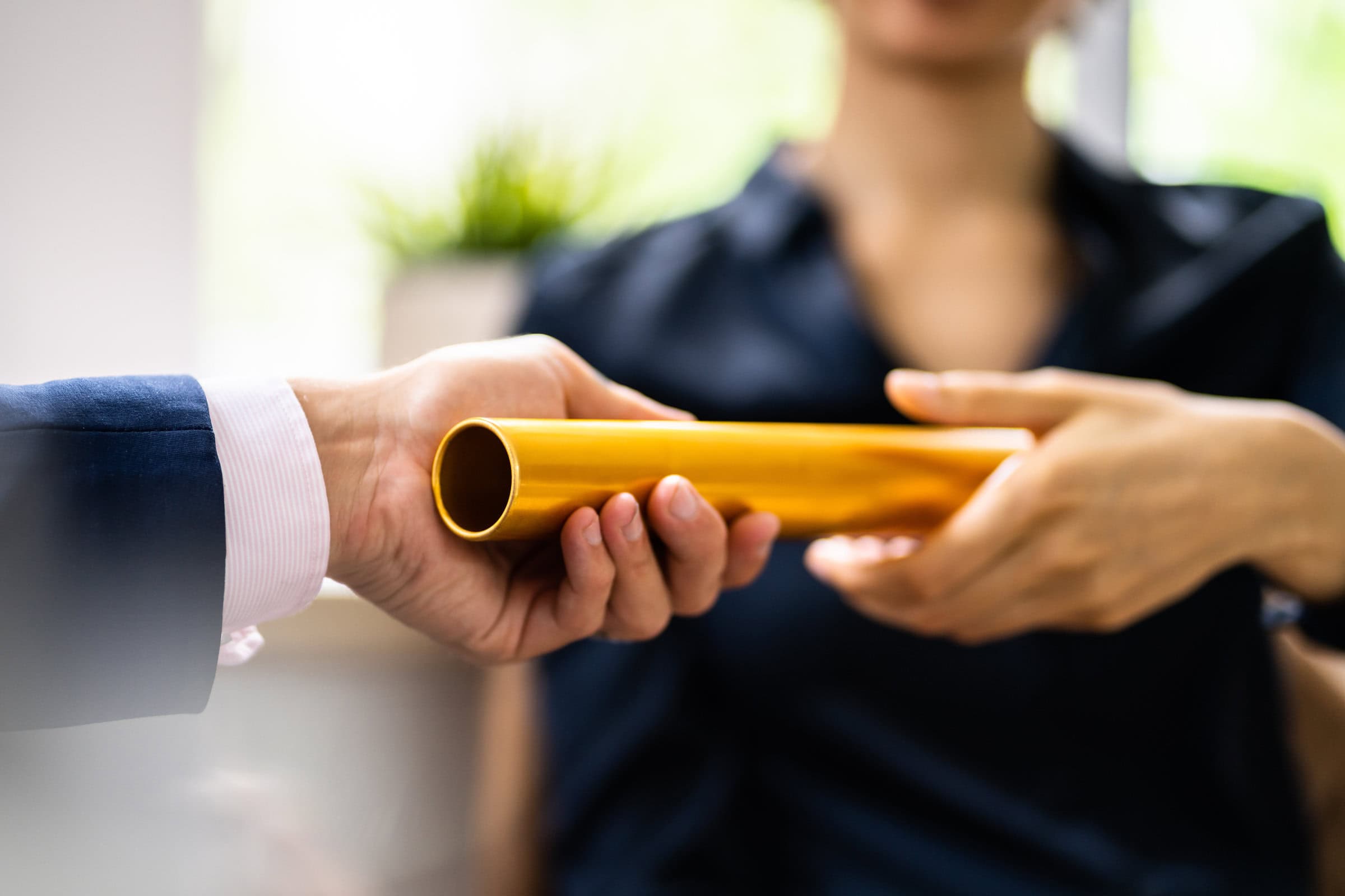 Close-up Of Businessman's Hand Passing The Golden Baton To His Partner In Office