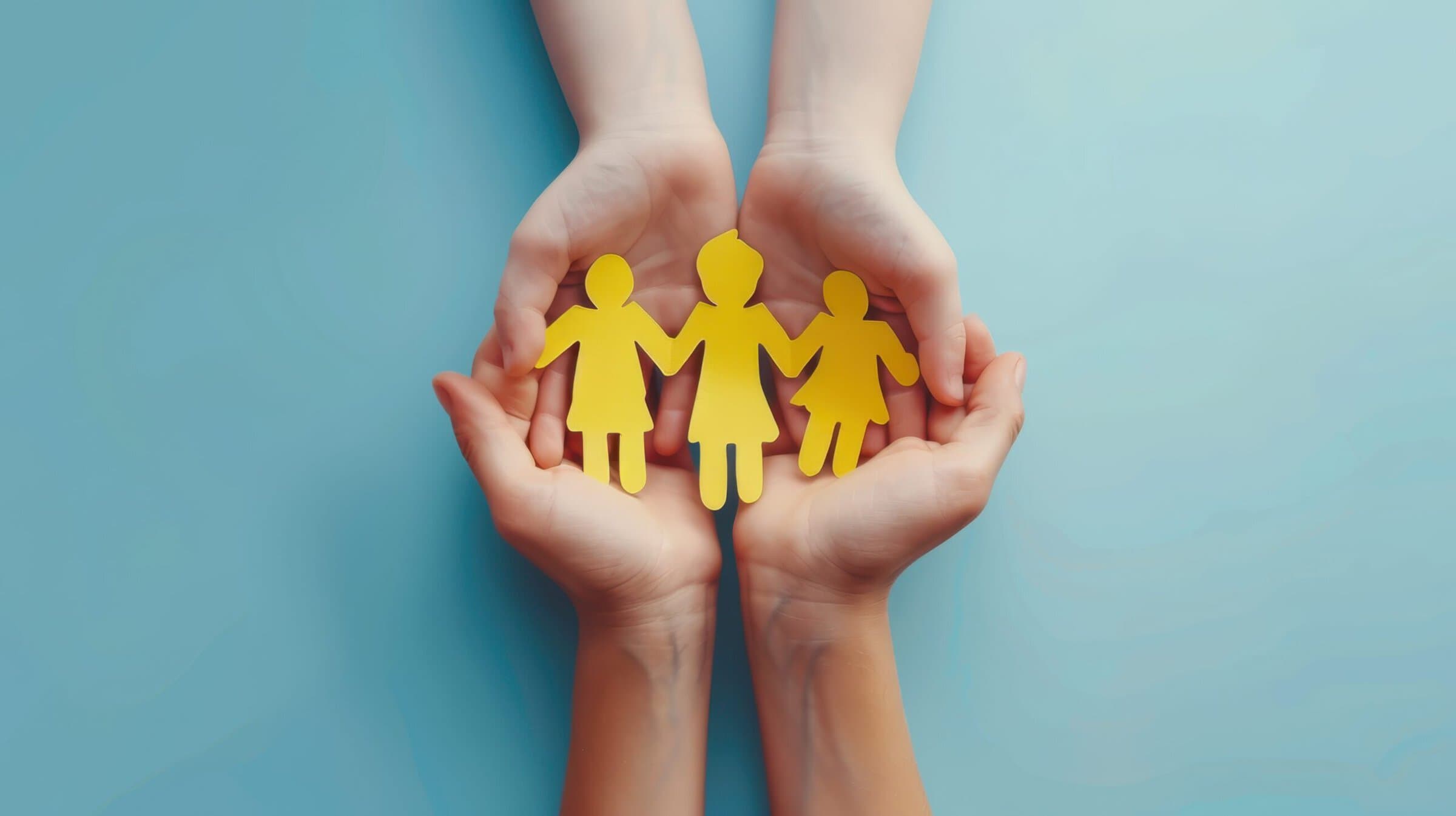 Adult and child hands holding yellow paper cutout figures of children.