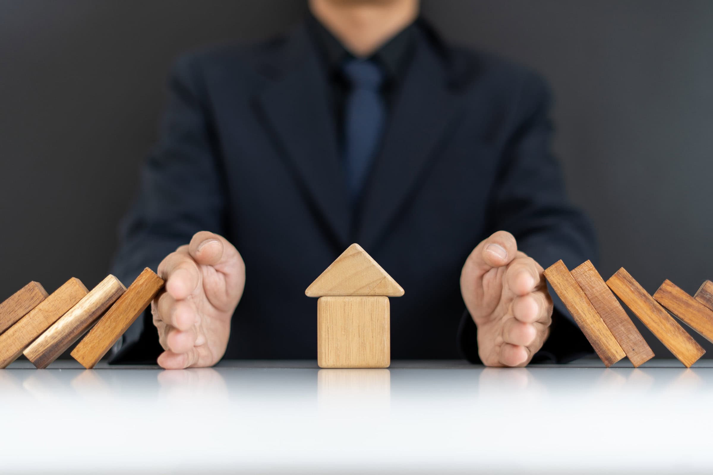 The concept of home insurance.The hands of businessmen or homeowners that are blocking Domino's fall from home. Maintaining security and home safety