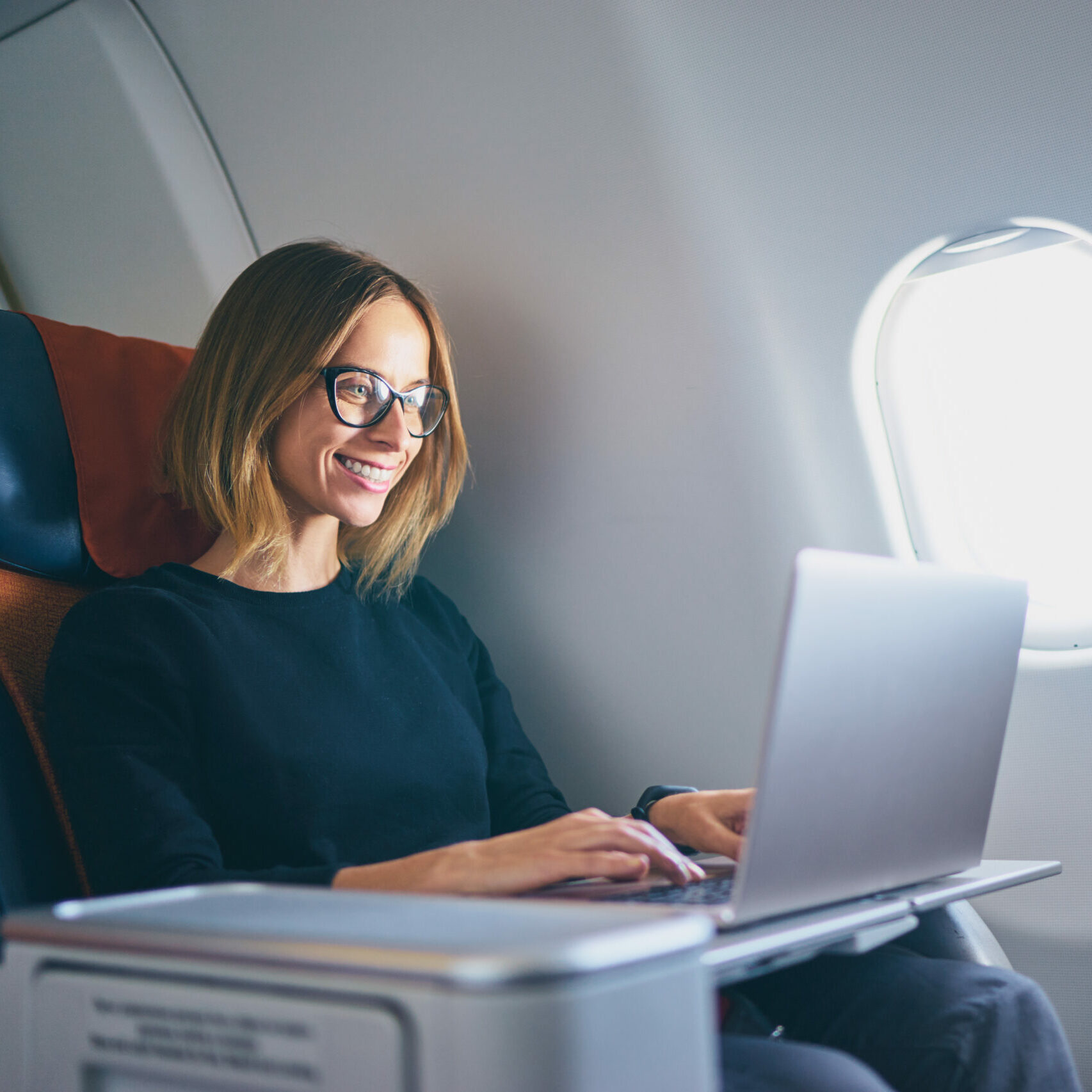 Traveling and technology. Flying at first class. Pretty young businees woman working on laptop computer while sitting in airplane.