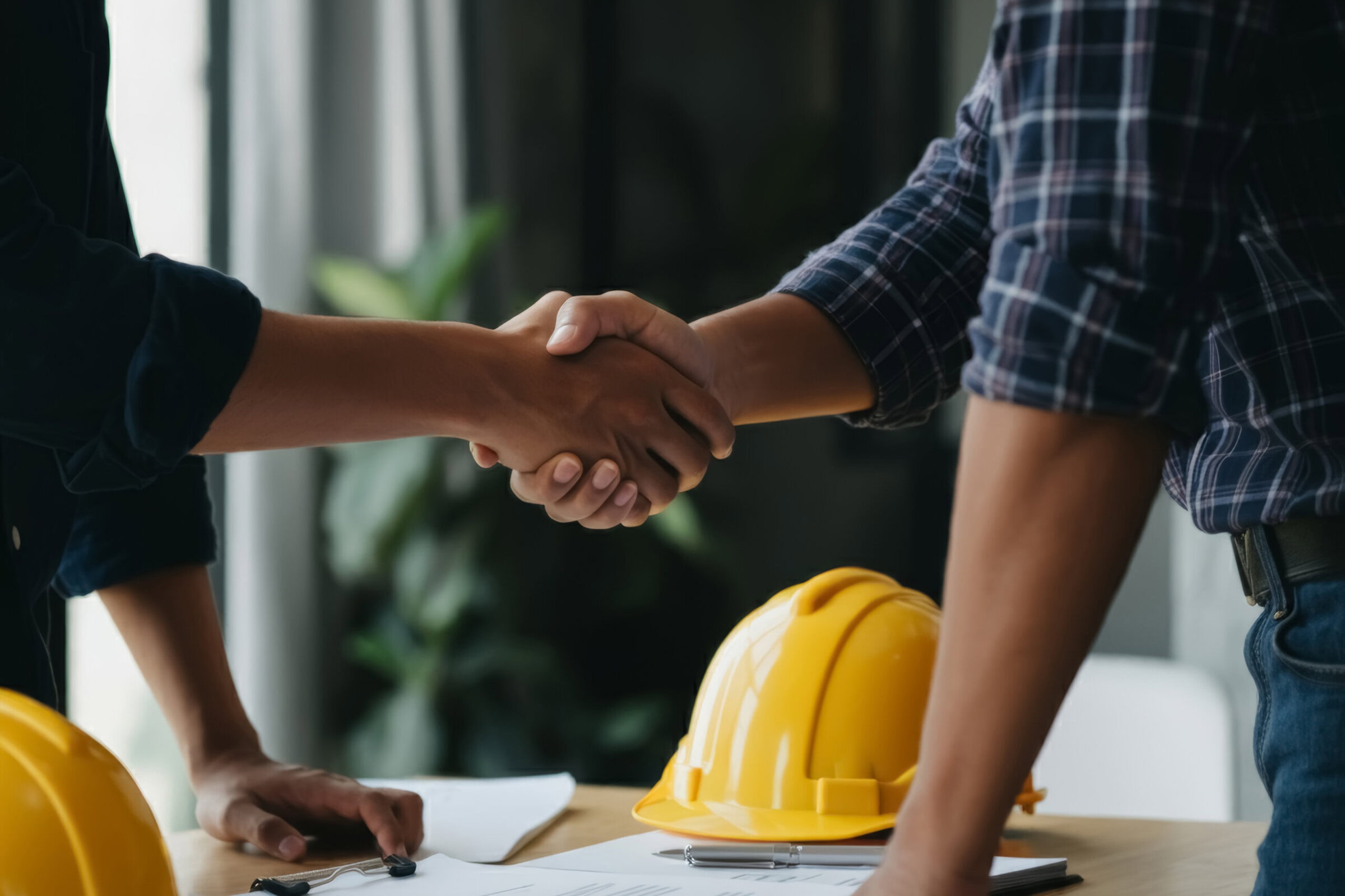 Construction team shaking hands to kick off a new project contract at the construction site office, symbolizing partnership and contracting. yellow safety helmet.