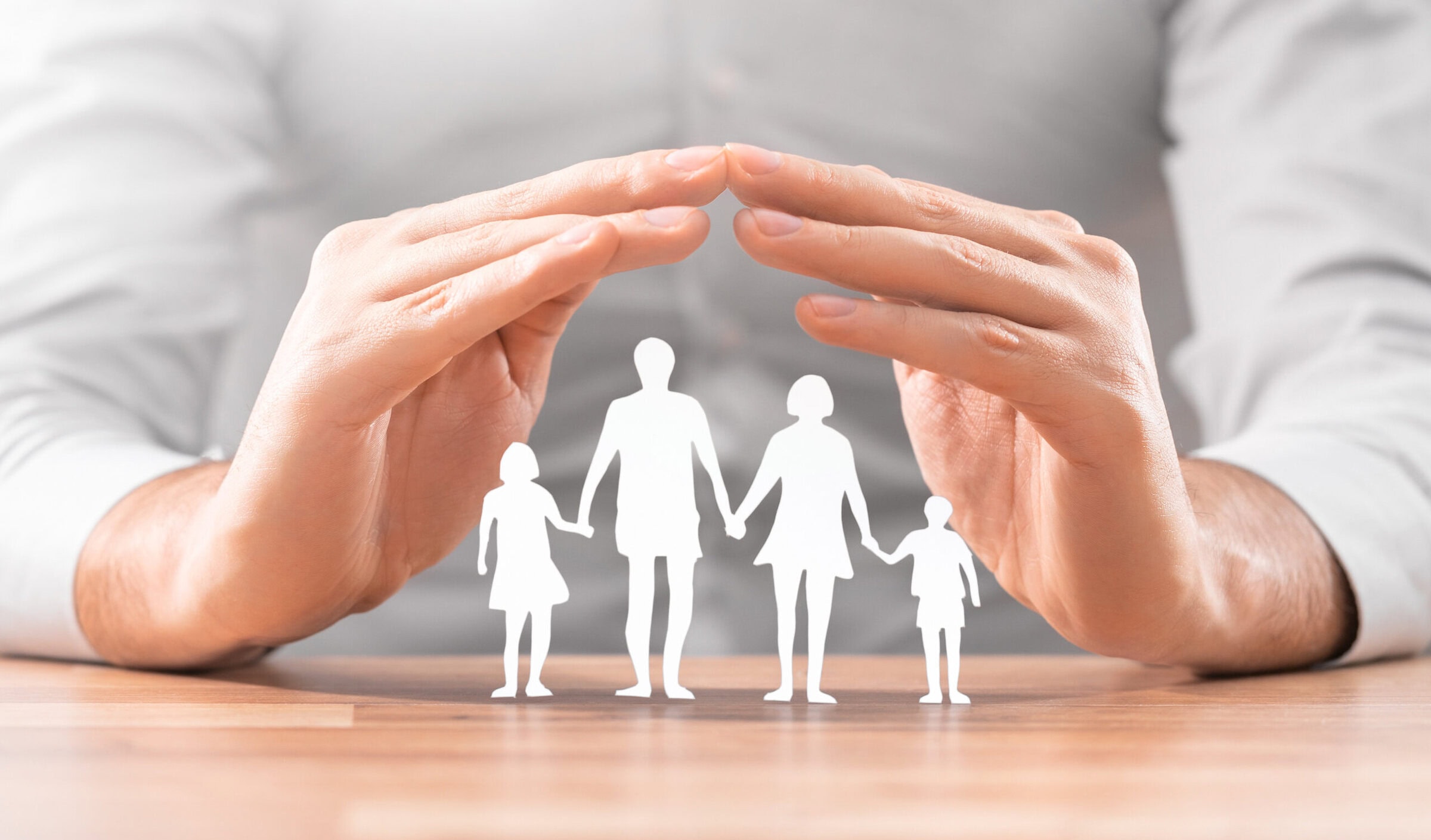 Hands with cut out paper silhouette on table. Family care concept.