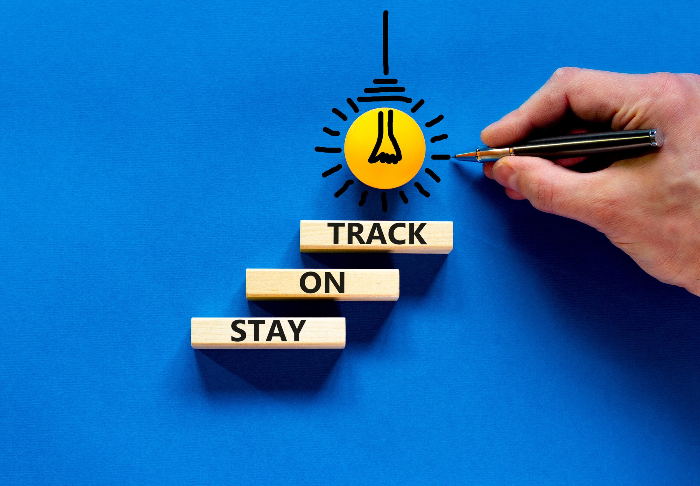 Stay on track symbol. Concept words Stay on track on wooden blocks on a beautiful blue table blue background. Businessman hand. Business, motivational and stay on track concept. Copy space.