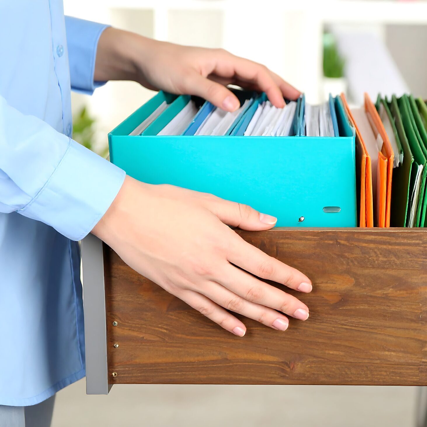 Person organizing colorful files in office drawer for efficient document management and improved workflow in a bright and organized workspace.