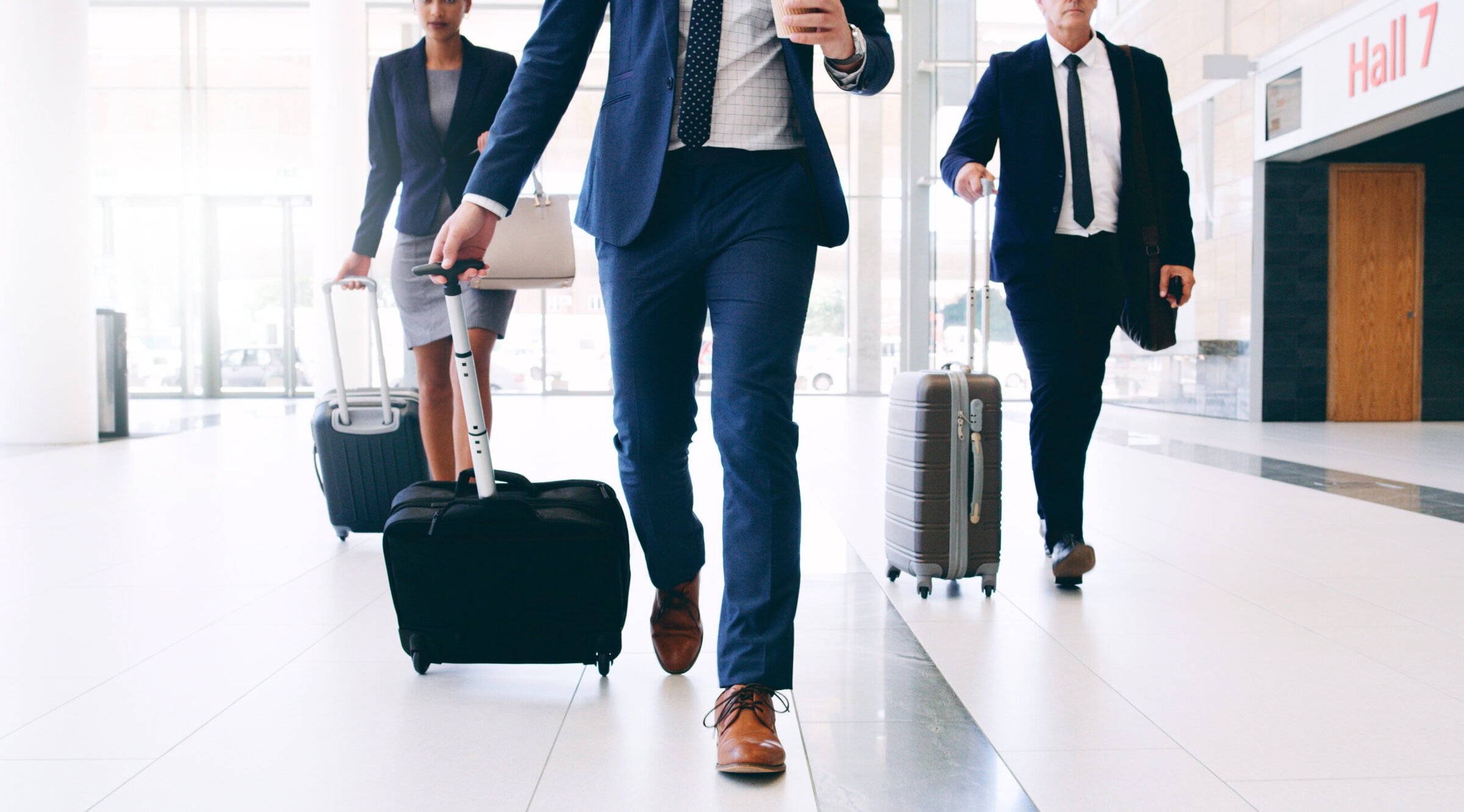 Cropped shot of three unrecognizable businesspeople walking and pulling suitcases while in the office during the day.