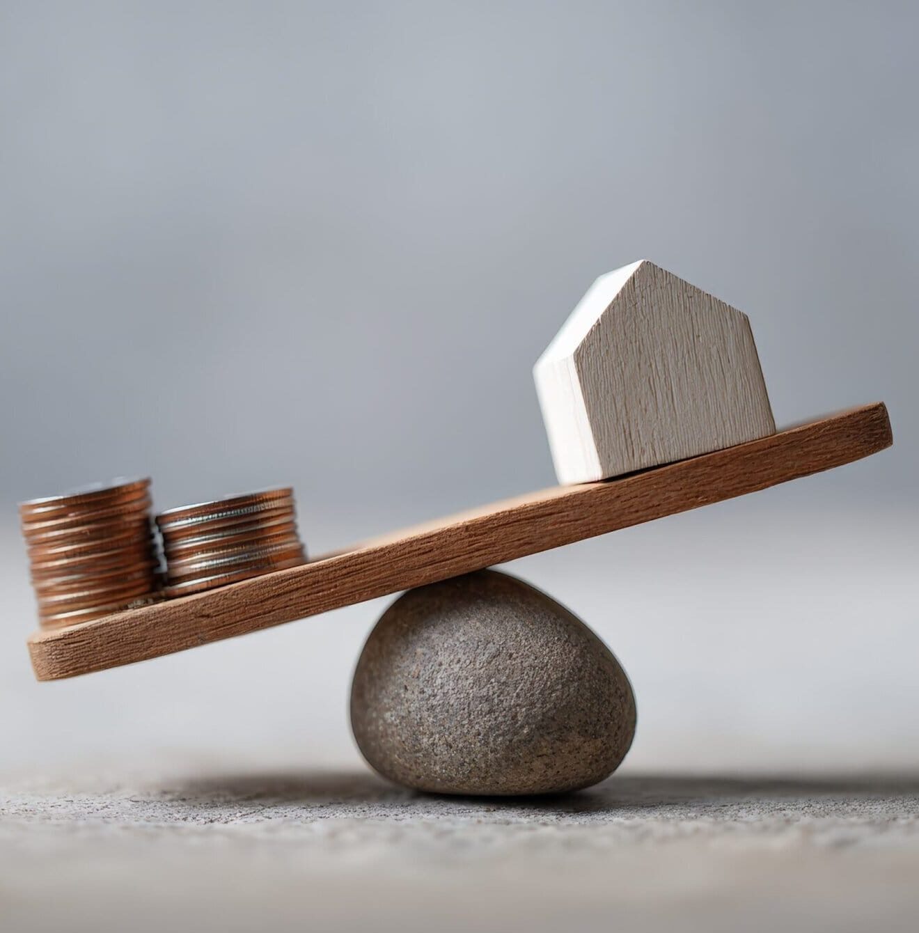 Miniature house and stacked coins balancing on a wooden seesaw, symbolizing the delicate balance of real estate investment, mortgage payments, and housing expenses in the current market