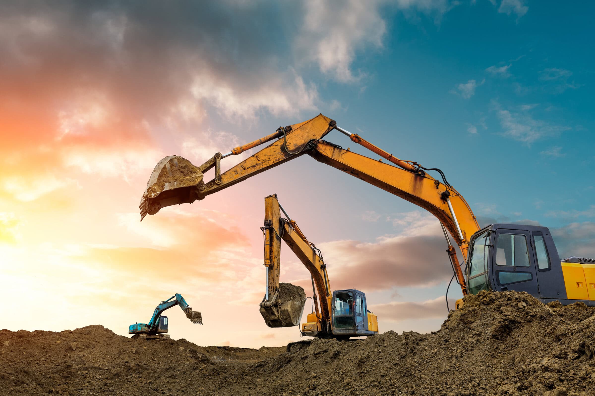 Three excavators work on construction site at sunset