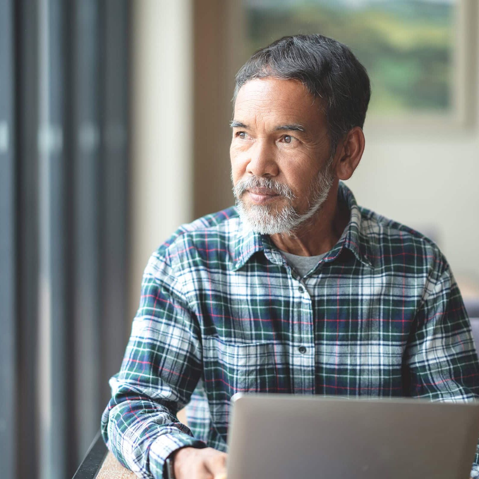 Mature man with white stylish short beard looking outside window. Casual lifestyle of retired hispanic people or adult asian man thinking and feeling confident sitting at modern coffee shop cafe.