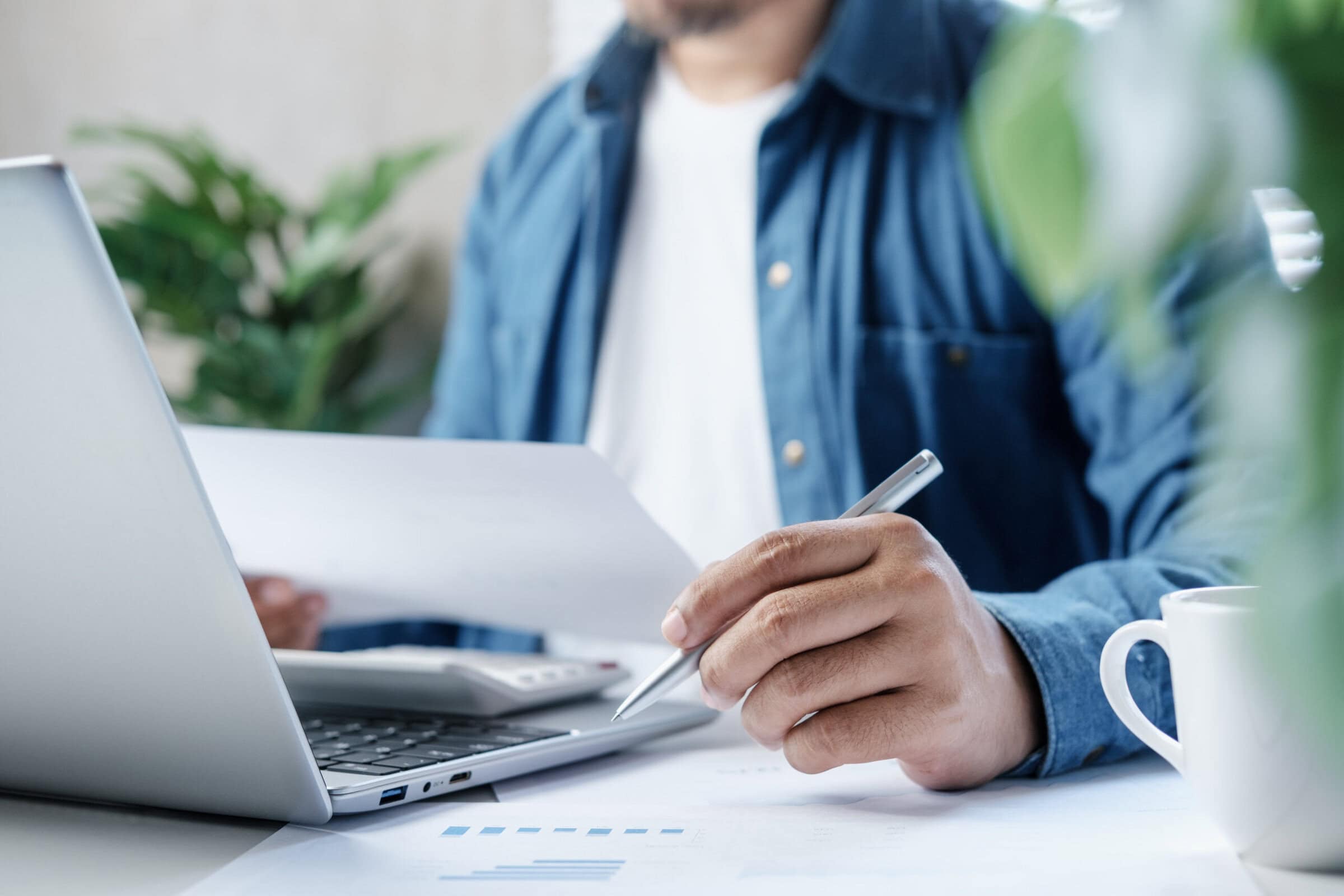 Business professional reviewing financial documents and calculating expenses on laptop with calculator at desk, personal finance management, accounting analysis and budget planning in modern workspace